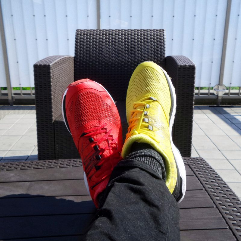 image depicts a persons crossed feet with one red trainer and one yellow trainer on