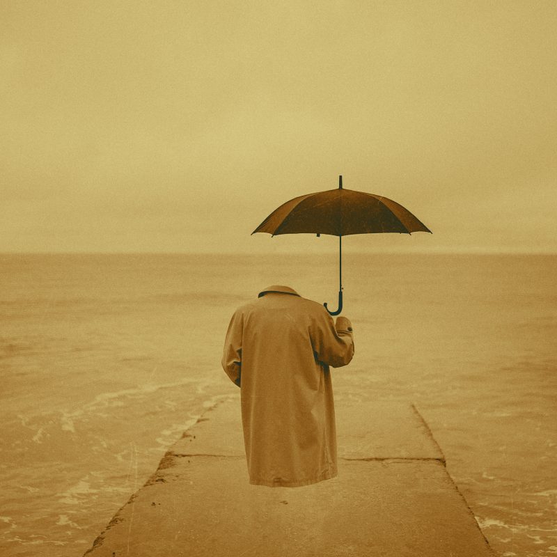 image is hsowing an invisable man with a floating coat and umbrella but no body. by the sea.