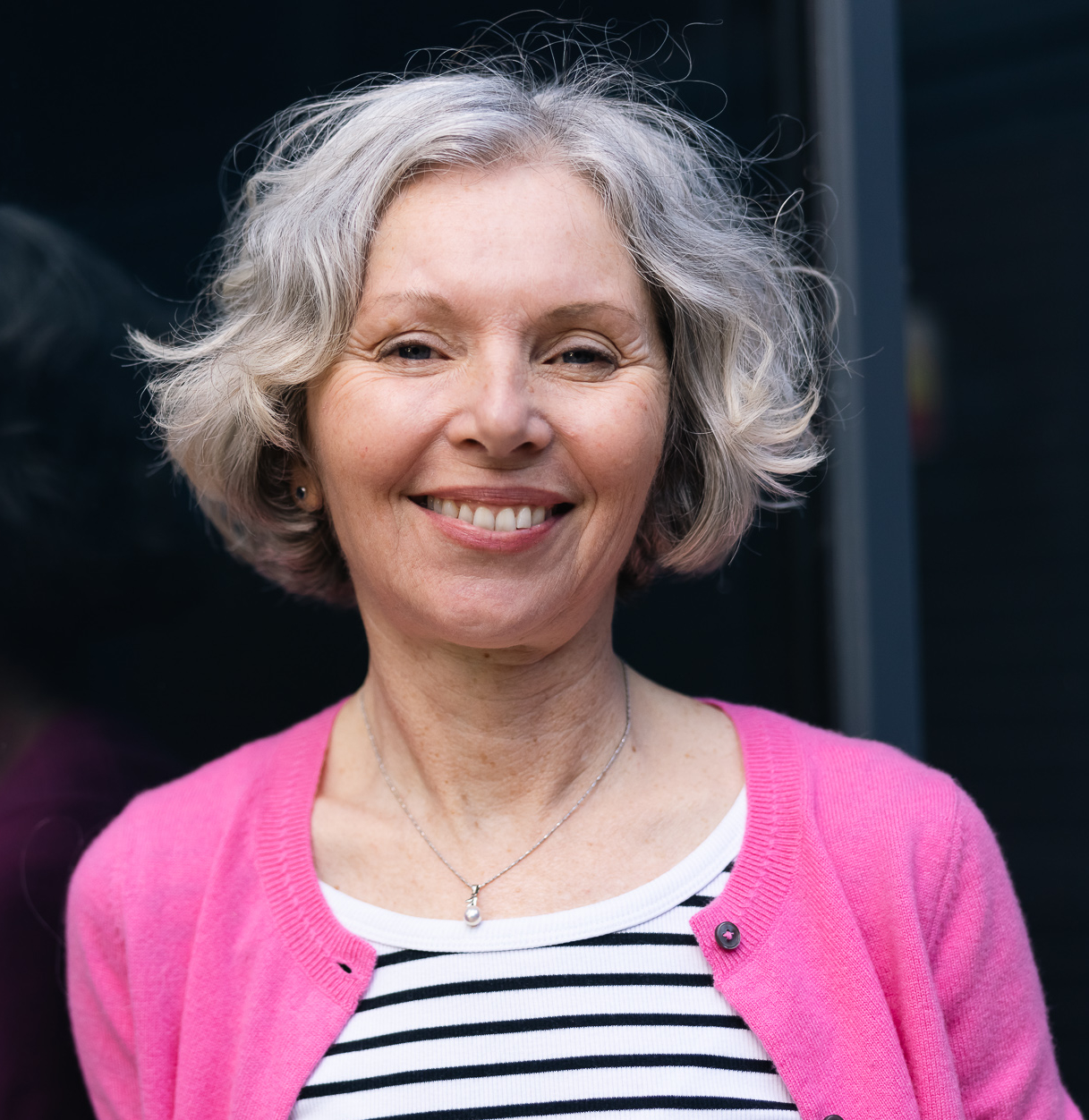 white woman with white bobbed hair smiling wearing a pink jumper