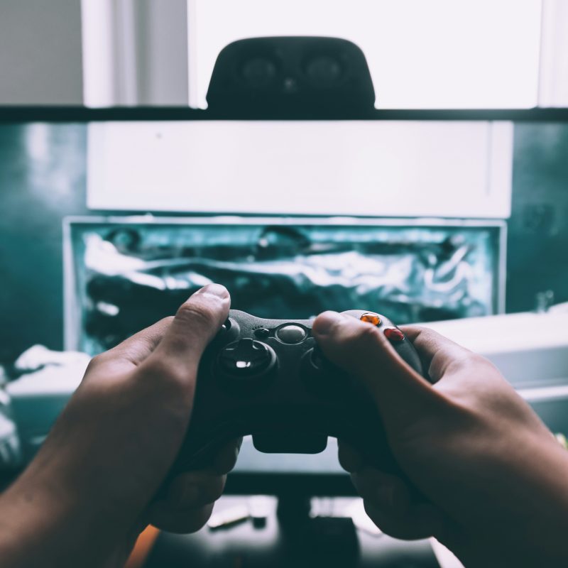 Hands holding a gaming controller in front of a computer monitor